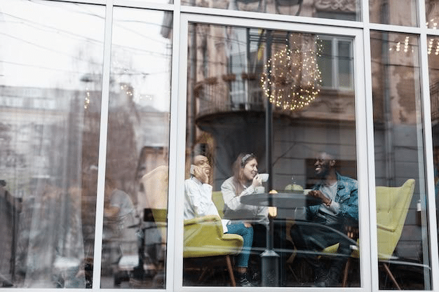 Three female friends sitting in a restaurant sipping coffee as seen through its glass window