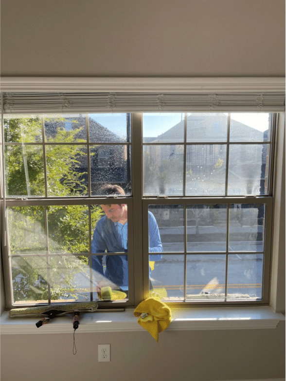 A professional cleaner seen through the glass from inside, wiping the exterior of a commercial window.