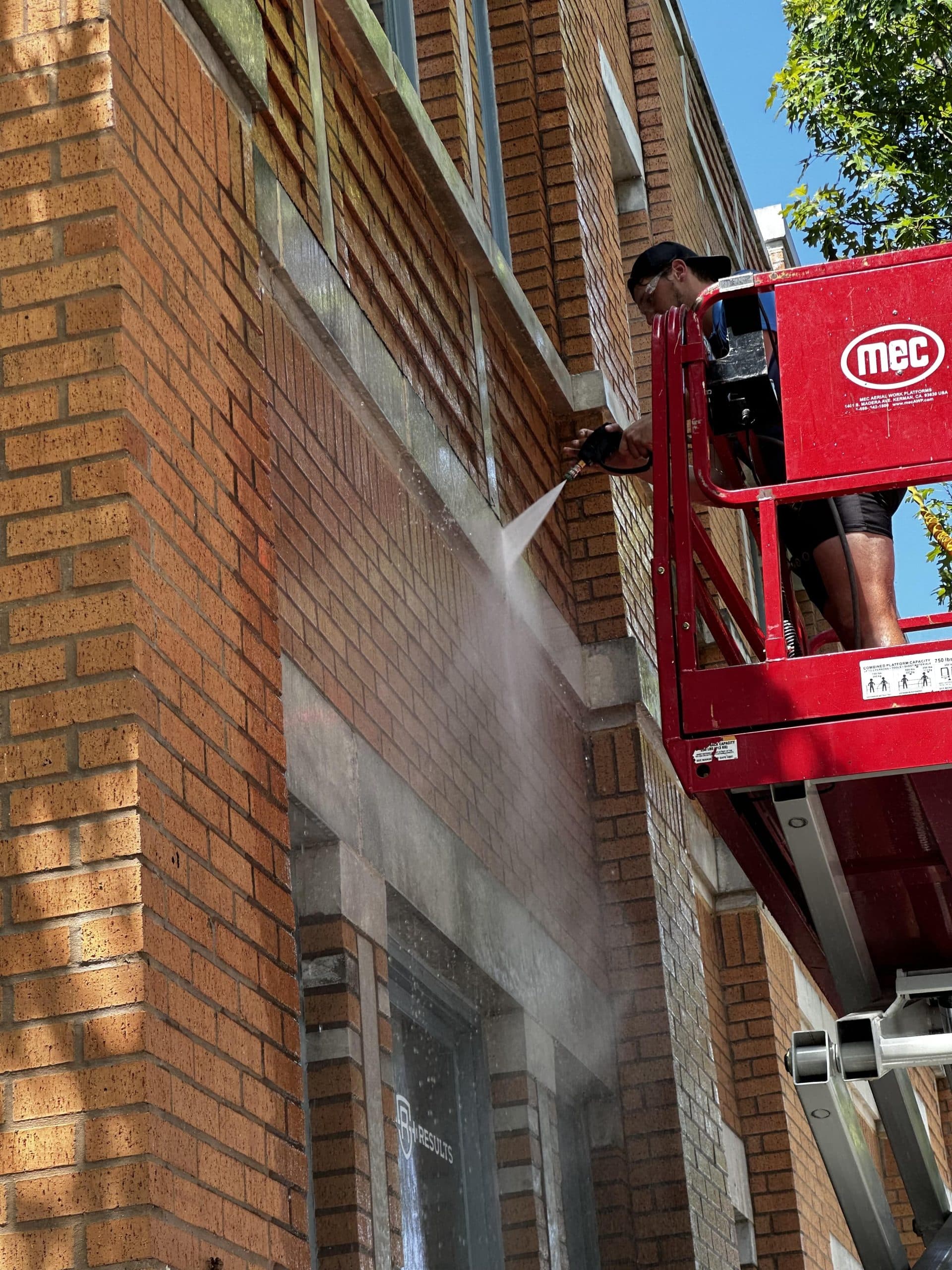 A professional pressure washing technician on a crane cleaning the exterior of a commercial building in Westlake, TX.