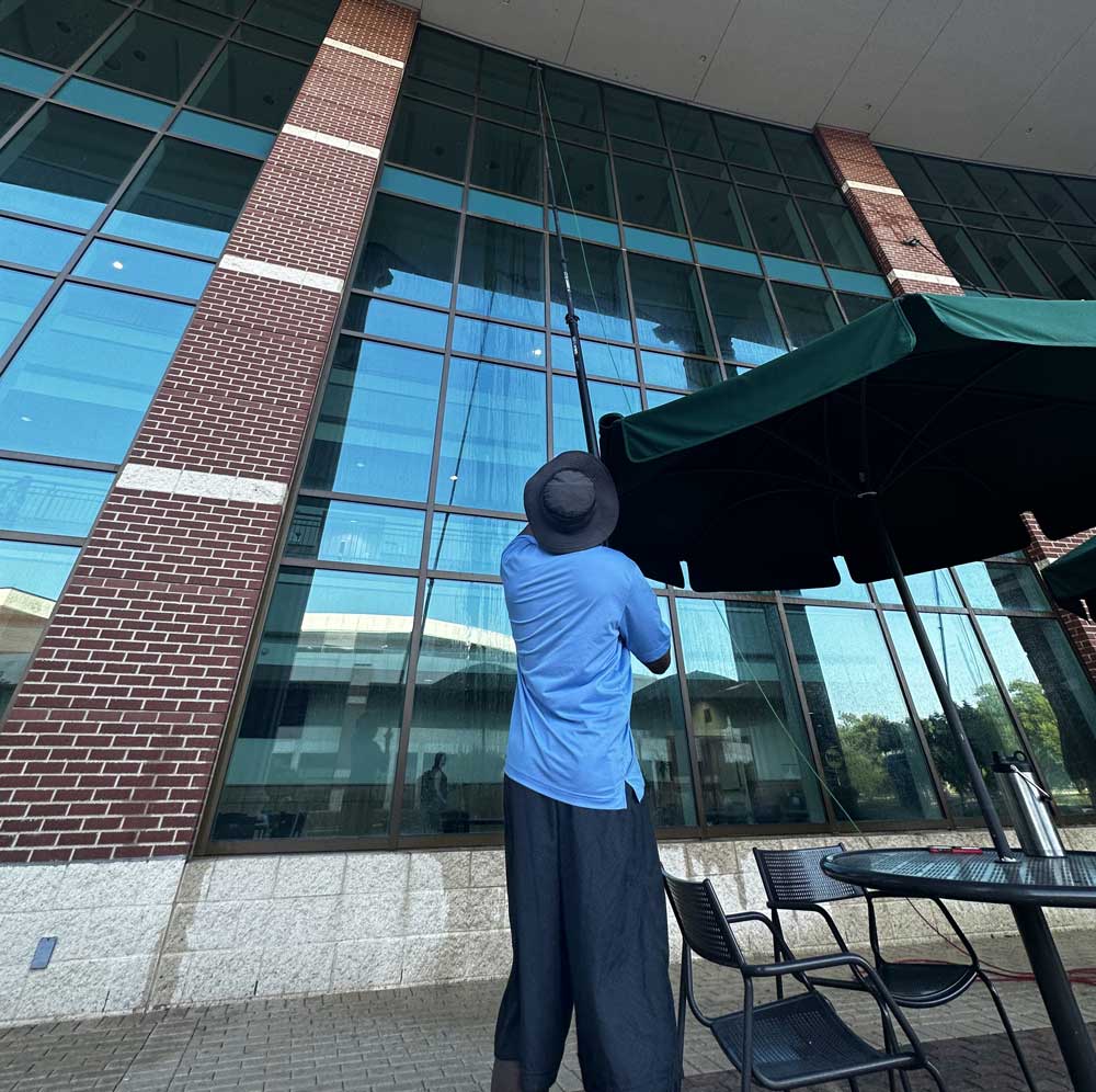 Professional technician performing commercial window cleaning services on a brick office building in Dallas.